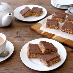 Three squares of Rice Crispy peanut bars on a tea table. There is a teapot and a cup of tea alongside.