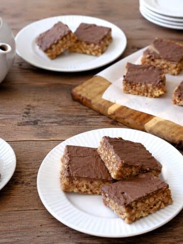 Three squares of Rice Crispy peanut bars on a tea table. There is a teapot and a cup of tea alongside.
