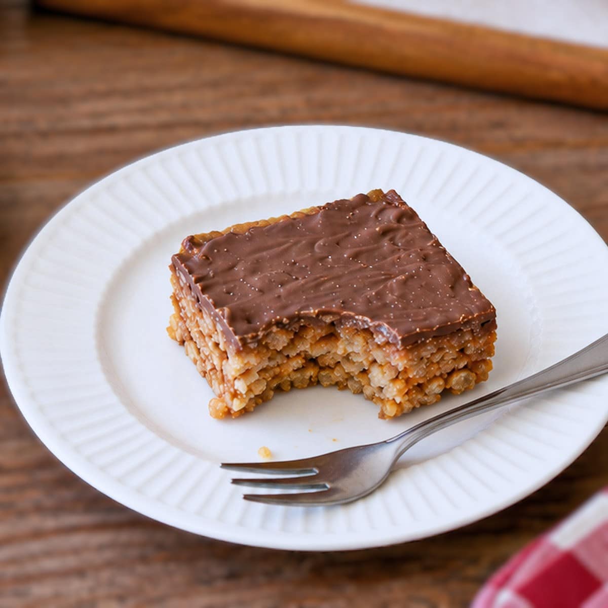 Close up of a square of Rice Krispie peanut slice on a white plate. There is a bite taken out of one corner.
