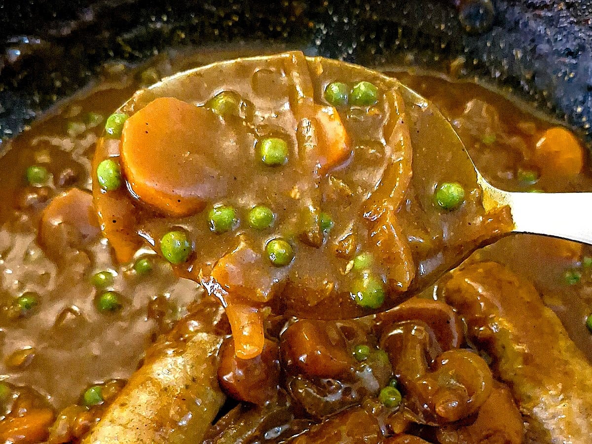 A spoonful of curried sauce, with onions, carrots and peas.