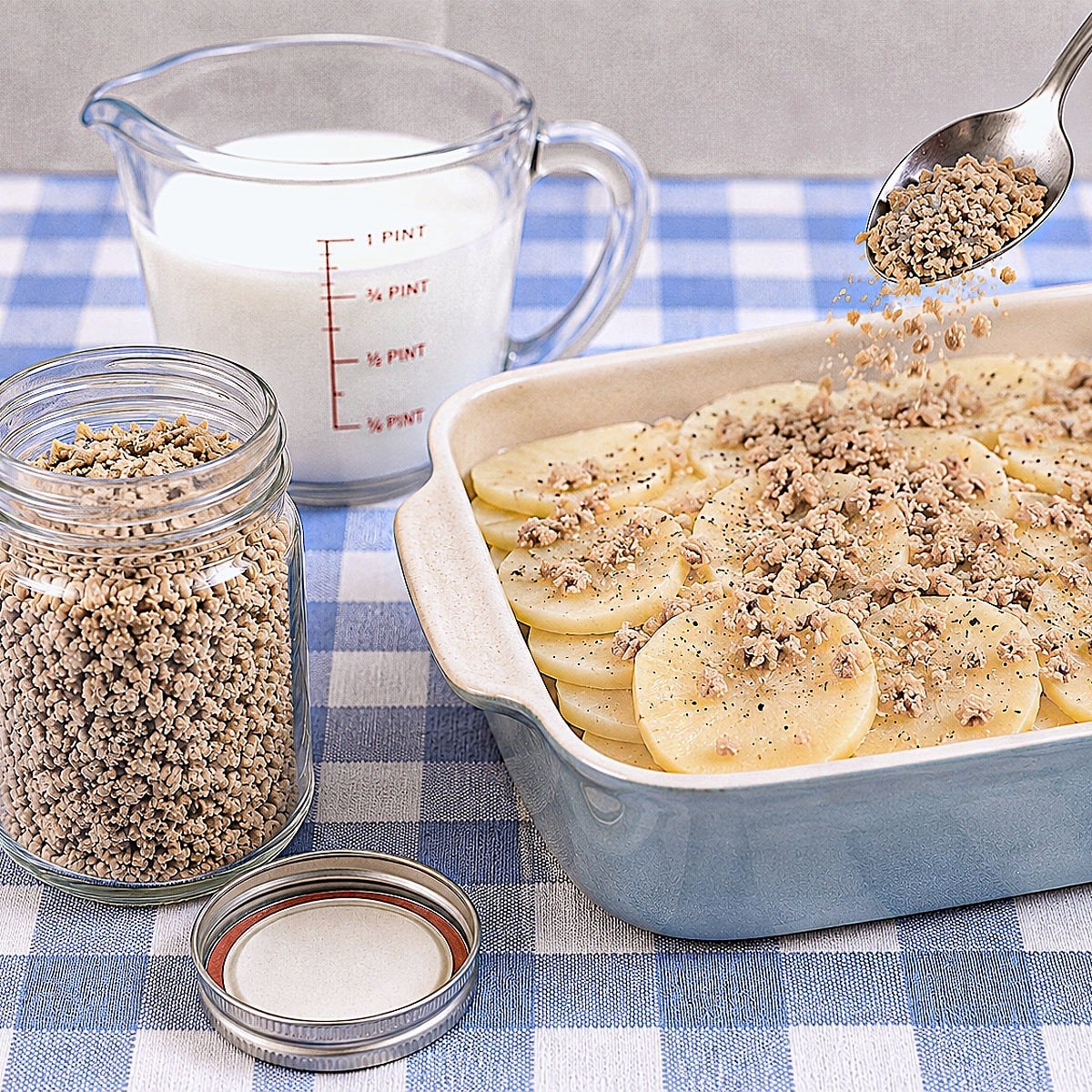 A spoonful of French onion seasoning mix being sprinkled over a dish of sliced potatoes.
