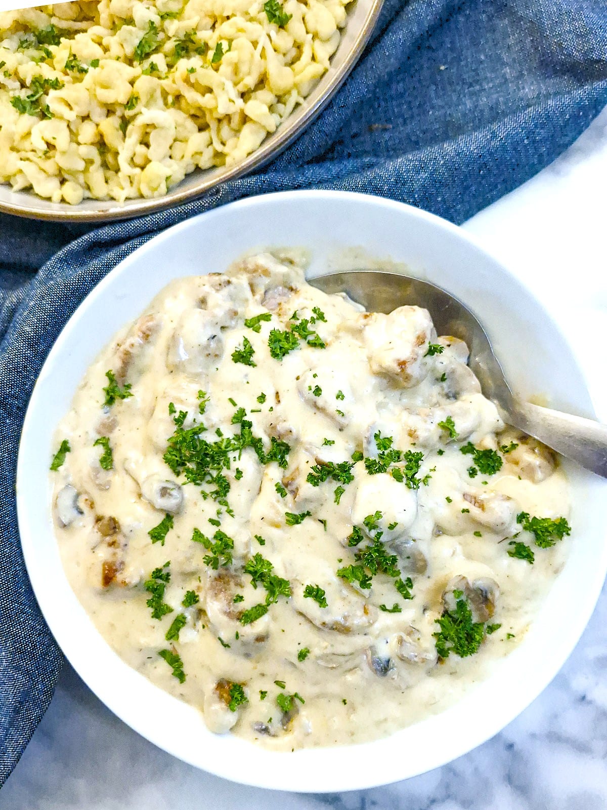 A large serving dish of rahmgeschnetzeltes. You can see the corner of a dish of homemade spaetzle in the top left corner of the image.
