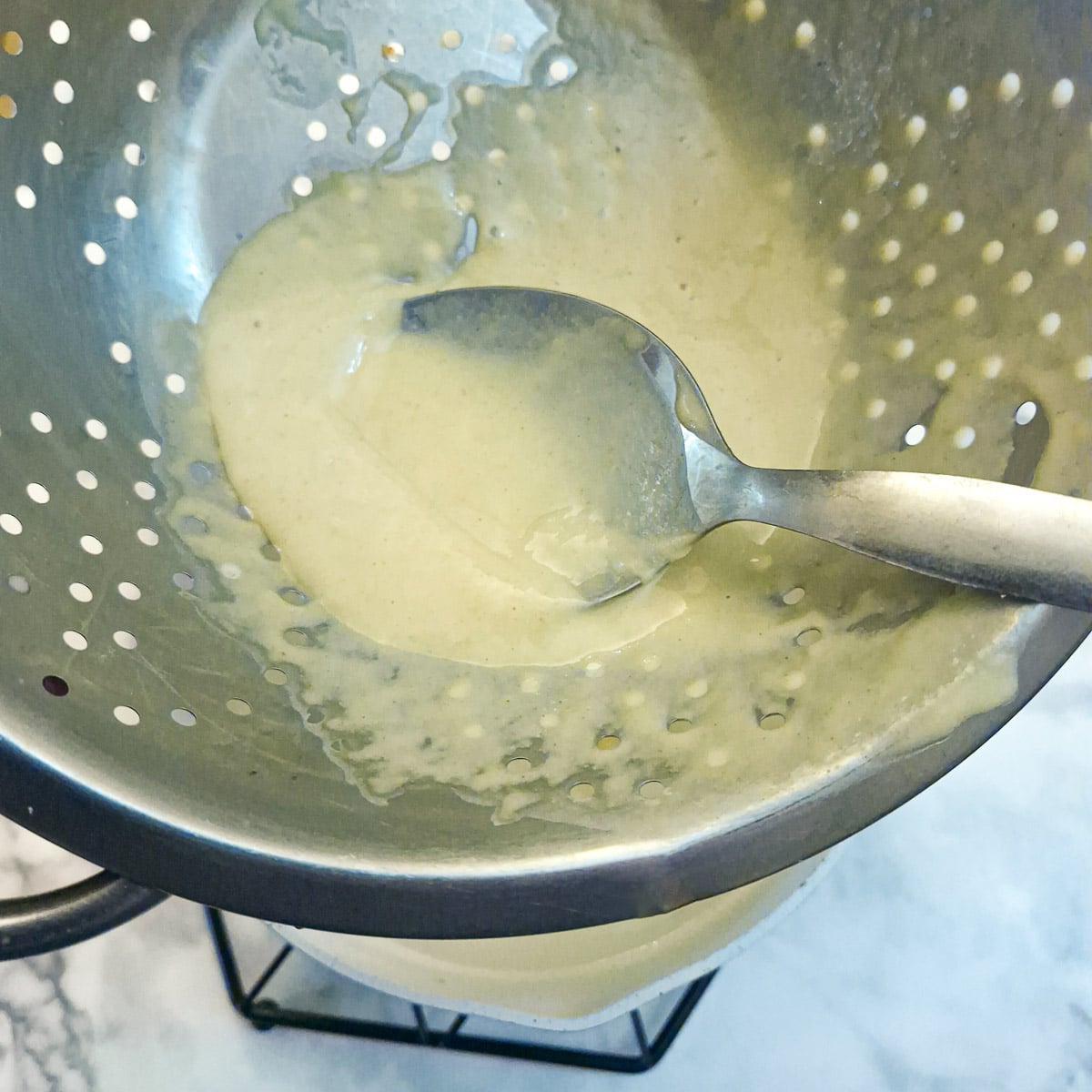 Step 4 - the spaetzle batter being pressed through the holes of a colander into a pan of boiling water.