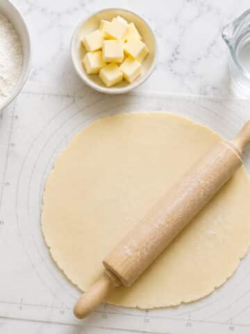 A ccircle of shortcrust pastry being rolled on a table.