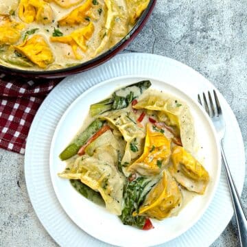 A white plate of gyoza in Thai green curry sauce next to the casserole dish.
