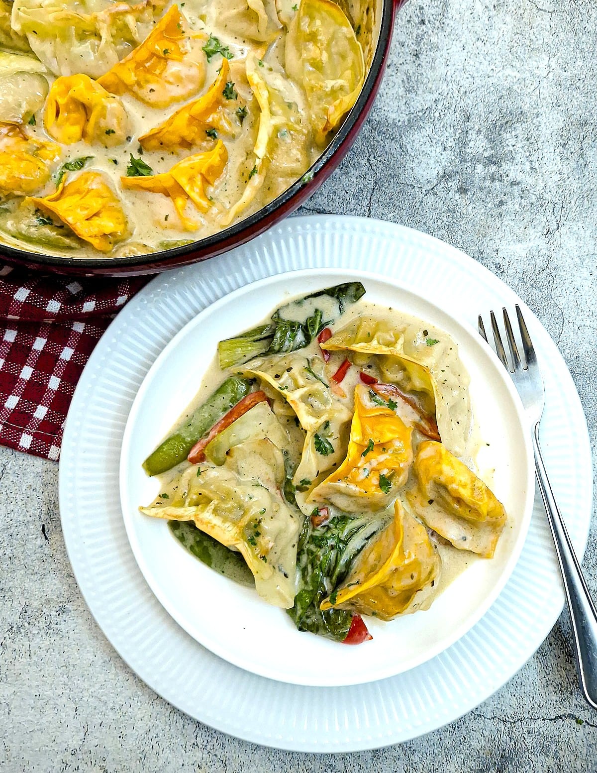 A white plate of gyoza in Thai green curry sauce next to the casserole dish.