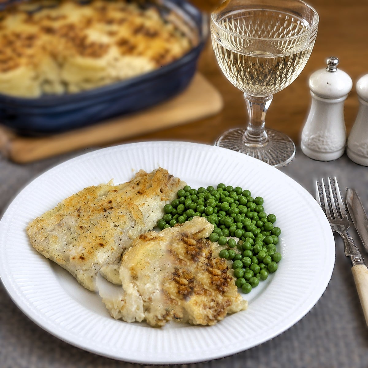A serving suggestion - a piece of lightly battered fish on a white plate with a helping of french onion potato bake and peas.