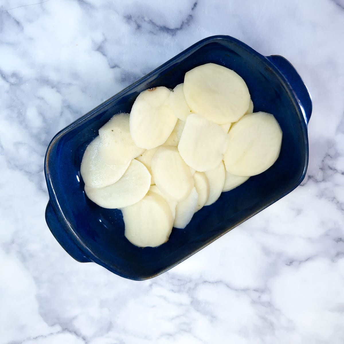 Step 1 - sliced potatoes arranged in a baking dish.