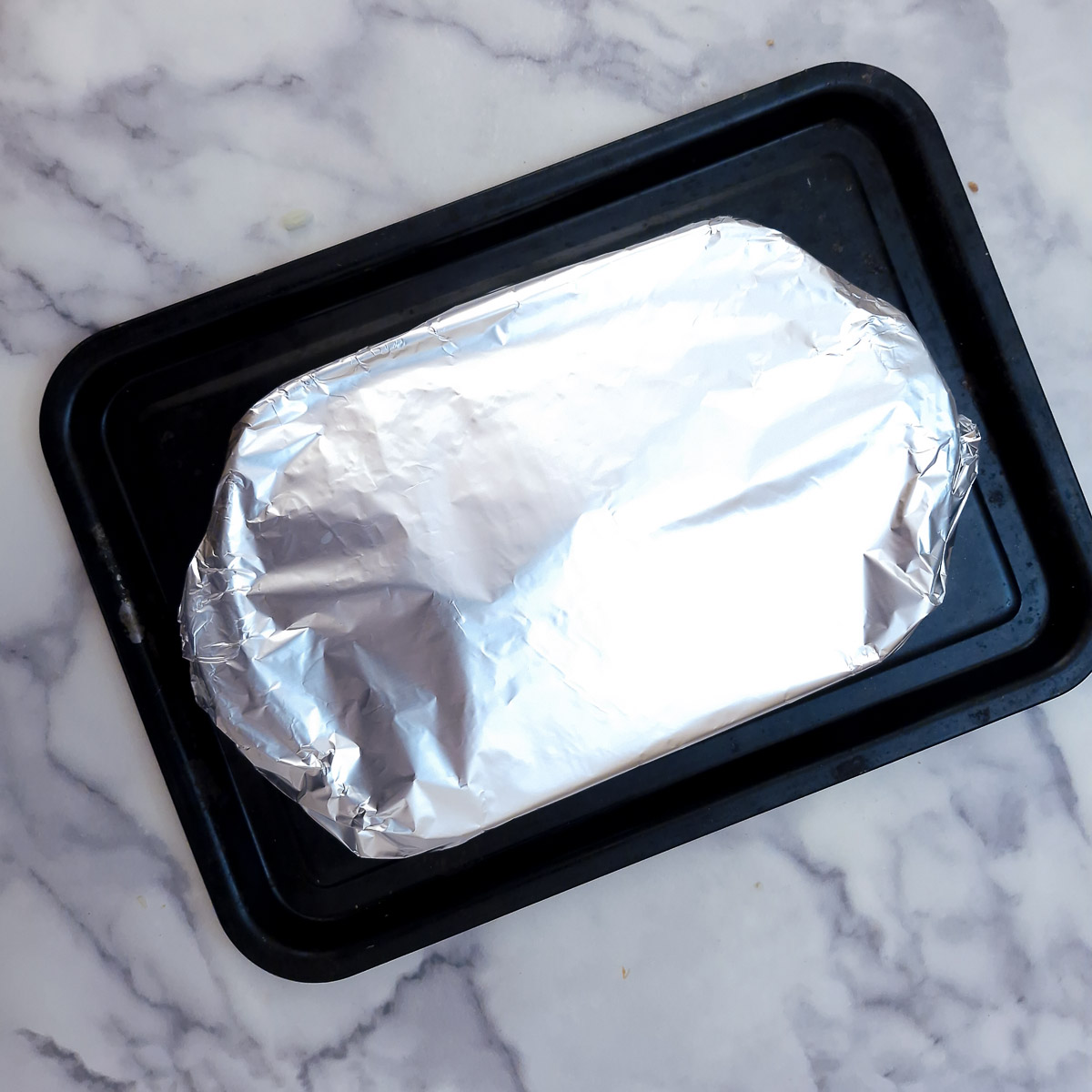 Step 6 - the potato bake covered with tin foil, standing on a baking tray ready to go into the oven.