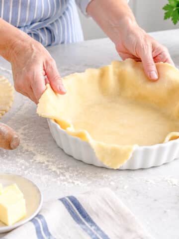 A pie dish being lined with shortcrust pastry.
