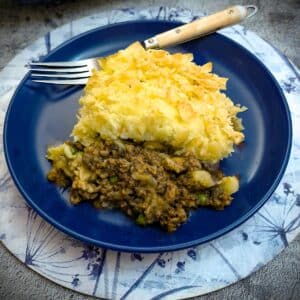 A serving of beef and mushroom bake on a plate showing the mince filling topped with crispy potatoes.
