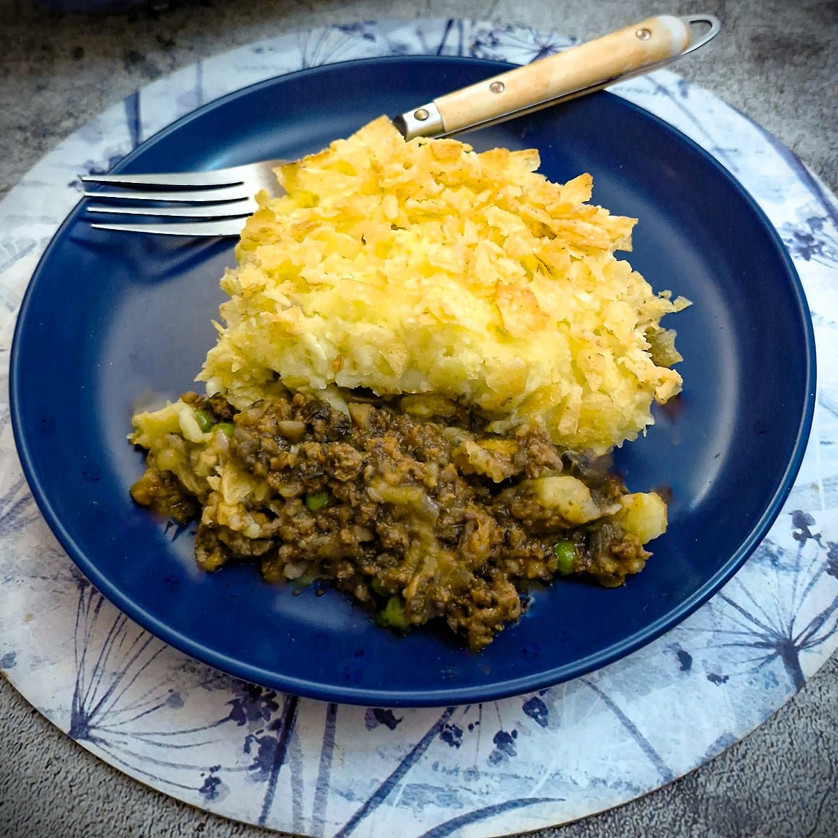 A serving of beef and mushroom bake on a plate showing the mince filling topped with crispy potatoes.