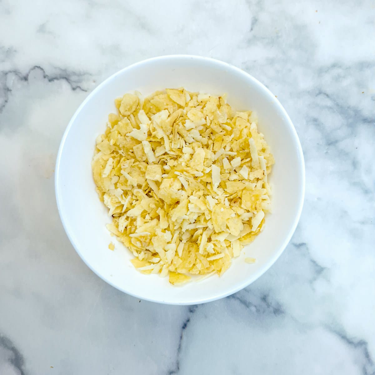 Step 9 - Grated cheese and crushed potato crisps in a small white bowl.