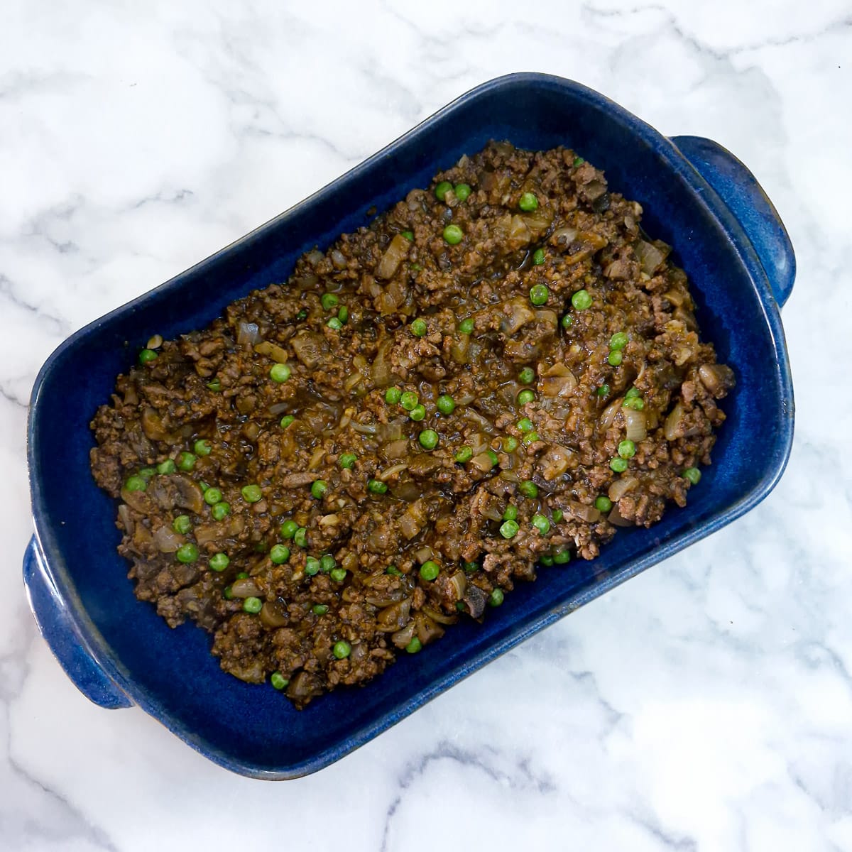 Step 8 - Half of the beef and mushroom mixture transferred into a blue casserole dish.